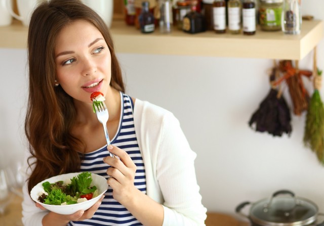 BM_Young woman eating salad and holding a mixed salad_90718075