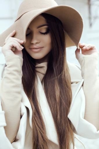 glamour girl with dark straight hair wears luxurious beige coat with elegant hat