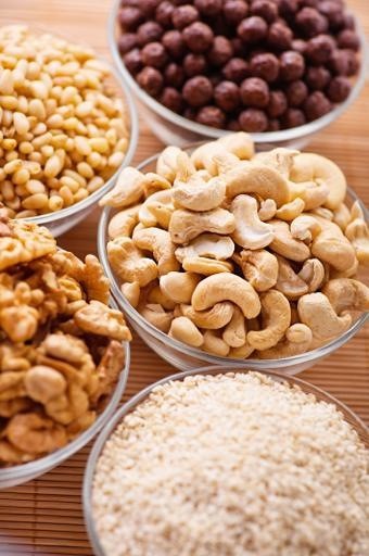 three bowls of peeled nuts (walnut, cashew, pine, sesame, chocolate balls) on background wooden table